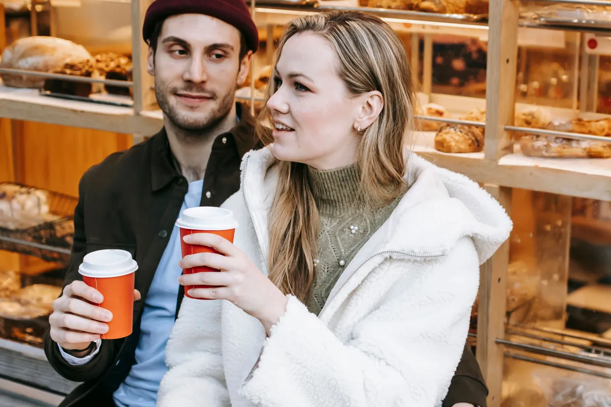Twee volwassenen praten met elkaar met een beker koffie in een bakkerij